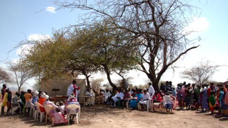 Baptism service taking place under the slim shade of acasia tree