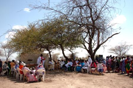 Baptism service taking place under the slim shade of acasia tree